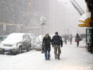 People walking down sidewalks in a snow storm in a city
